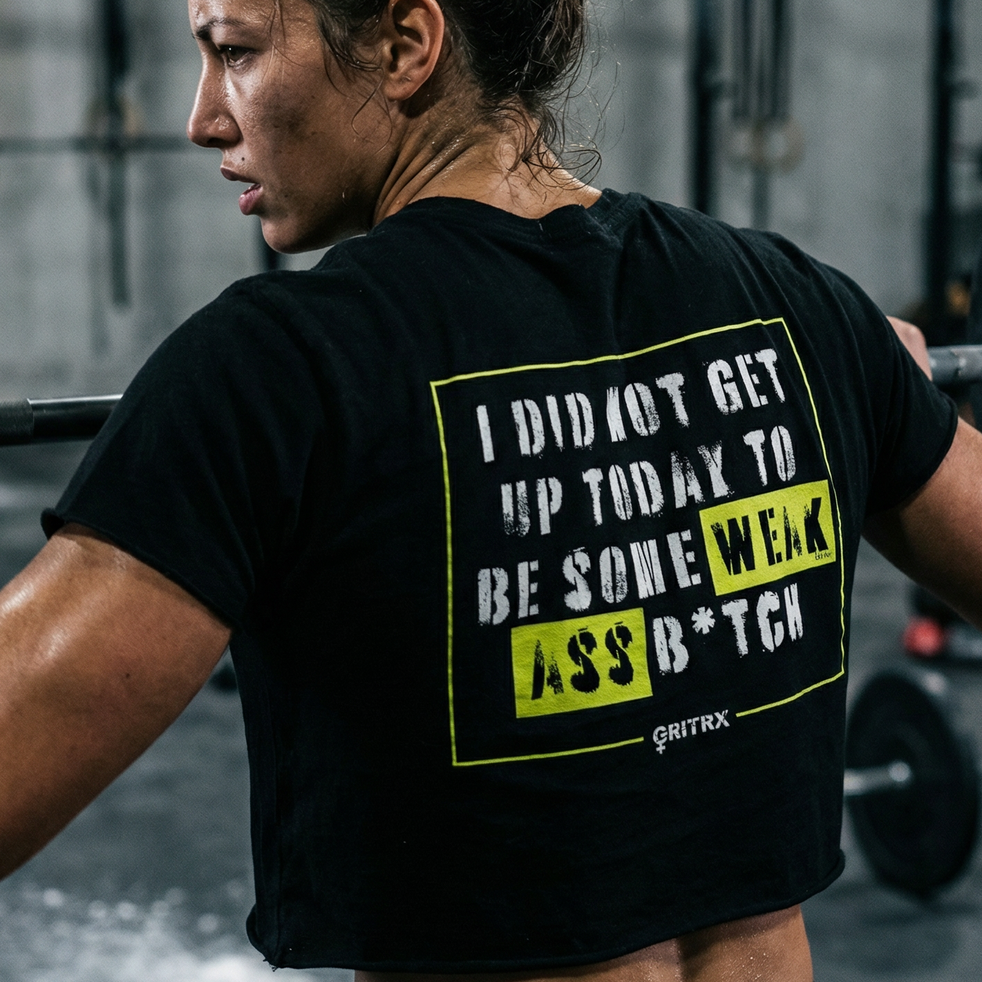 Woman lifting weights with a motivational quote on her black t-shirt in a gym setting.